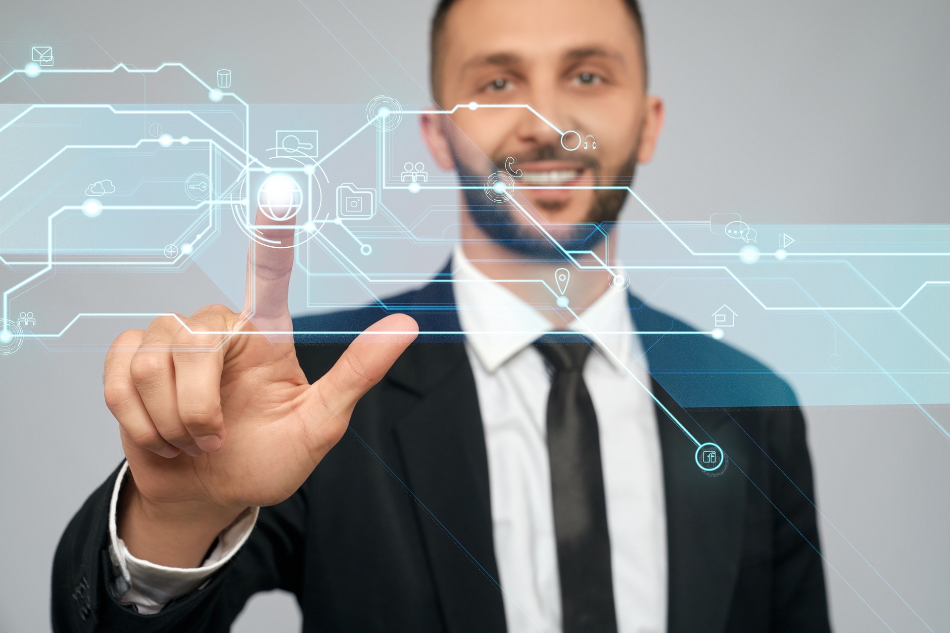 Front view of young smiling businessman in black suit in office. Selective focus of digital tactile charts screen, bearded man clicking virtual button. Concept of high technologies, digitalization.